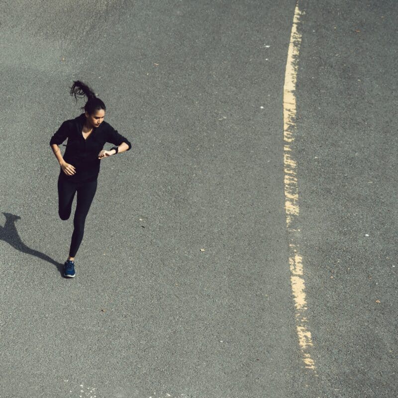 Een vrouw kijkt hardlopend op haar horloge - sneller hardlopen - RunX