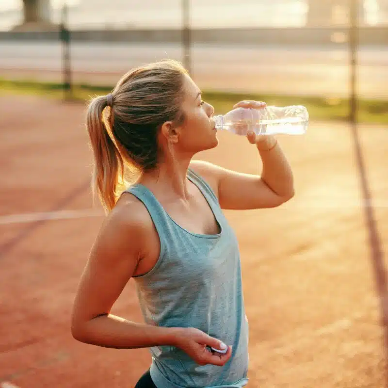 Woman takes a break during a run in hot weather and hydrates with a water bottle